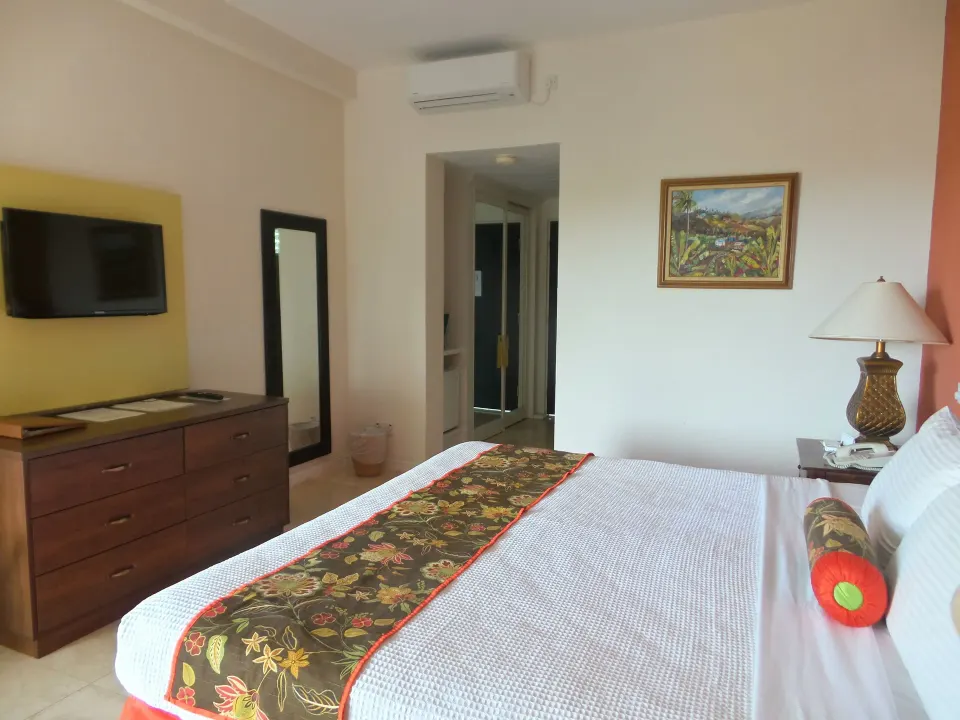 Superior Room king bed with dresser, TV, mirror, and hallway at Coyaba Beach Resort.