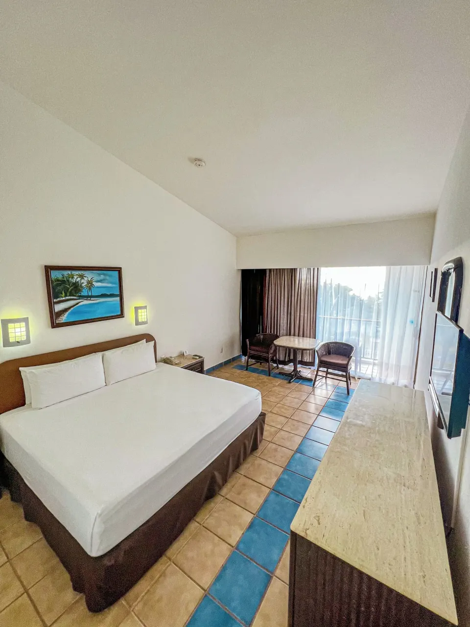 King bed and balcony access in a tiled guest room at Cozumel Hotel & Resort