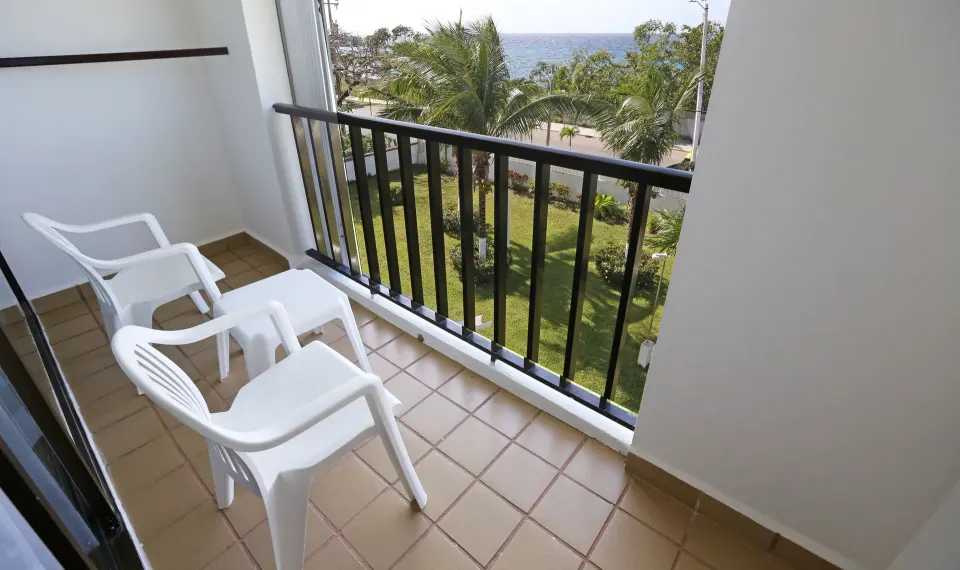 Small balcony with two plastic chairs and a view of palm trees and the sea at Cozumel Hotel & Resort