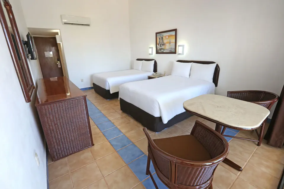 Twin beds, small dining table and dresser in a guest room at Cozumel Hotel & Resort