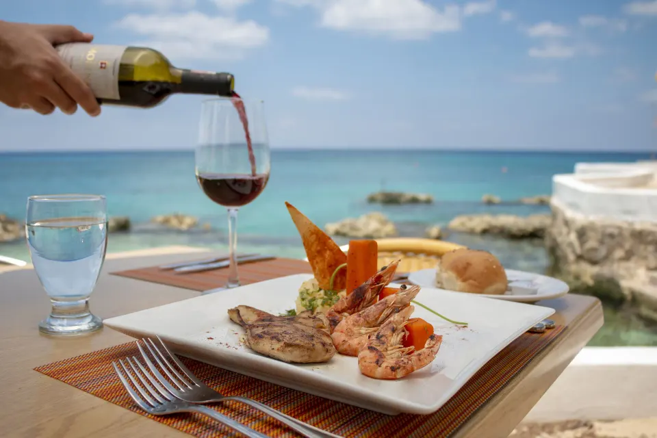 Seaside table with plated seafood and wine being poured at Cozumel Hotel & Resort