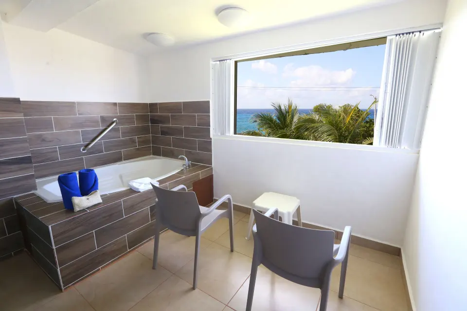 Jacuzzi tub and two chairs beside a window with ocean view at Cozumel Hotel & Resort