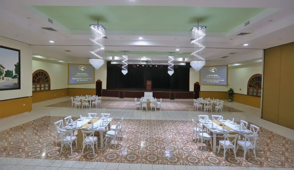 Wide view of the ballroom with tables and a stage at Cozumel Hotel & Resort