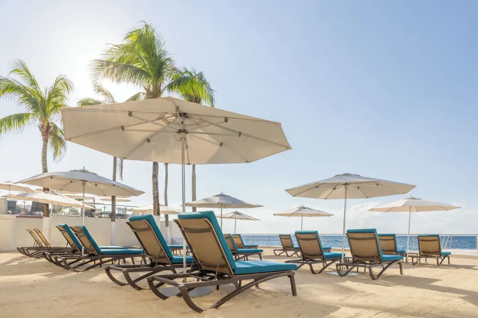 Beach loungers and umbrellas facing the ocean under palm trees at Cozumel Palace