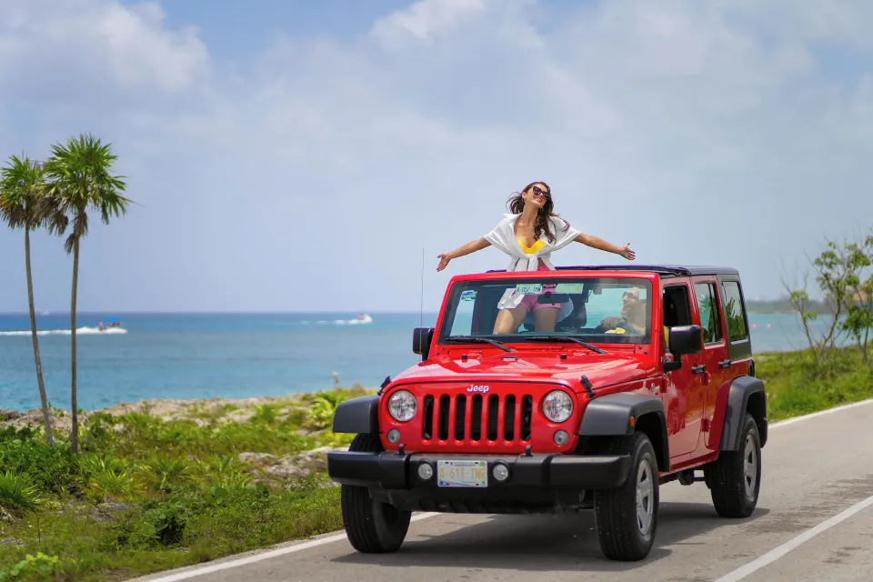 Red Jeep on coastal road with woman enjoying sun at Cozumel Palace
