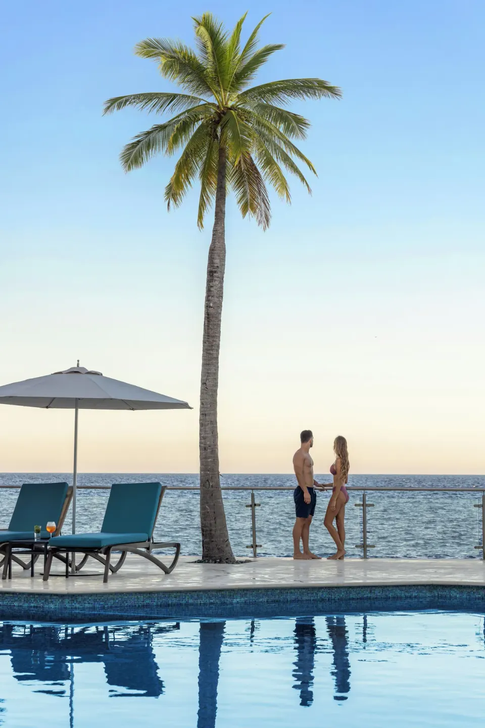 Couple standing near a palm tree beside the ocean at the Cozumel Palace pool edge