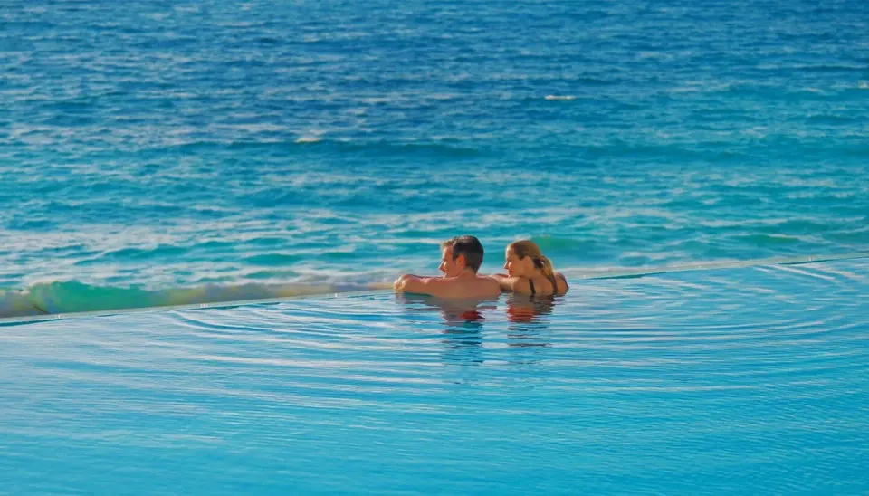 Couple leaning on the edge of an infinity pool overlooking turquoise ocean at Cozumel Palace