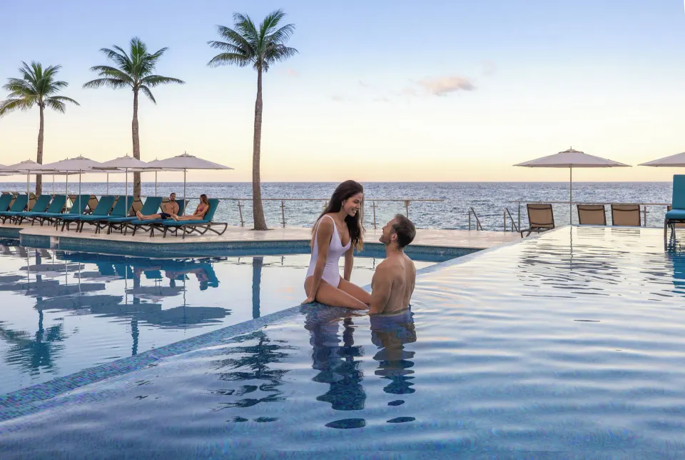 Couple in the infinity pool with loungers and ocean horizon at Cozumel Palace