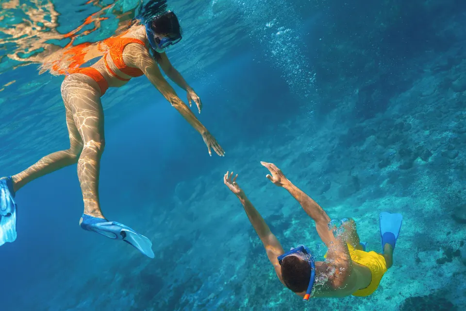 Two snorkelers reaching toward each other above a coral reef near Cozumel Palace