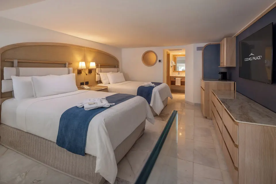 Guest room with two beds, TV and entry to bathroom at Cozumel Palace.