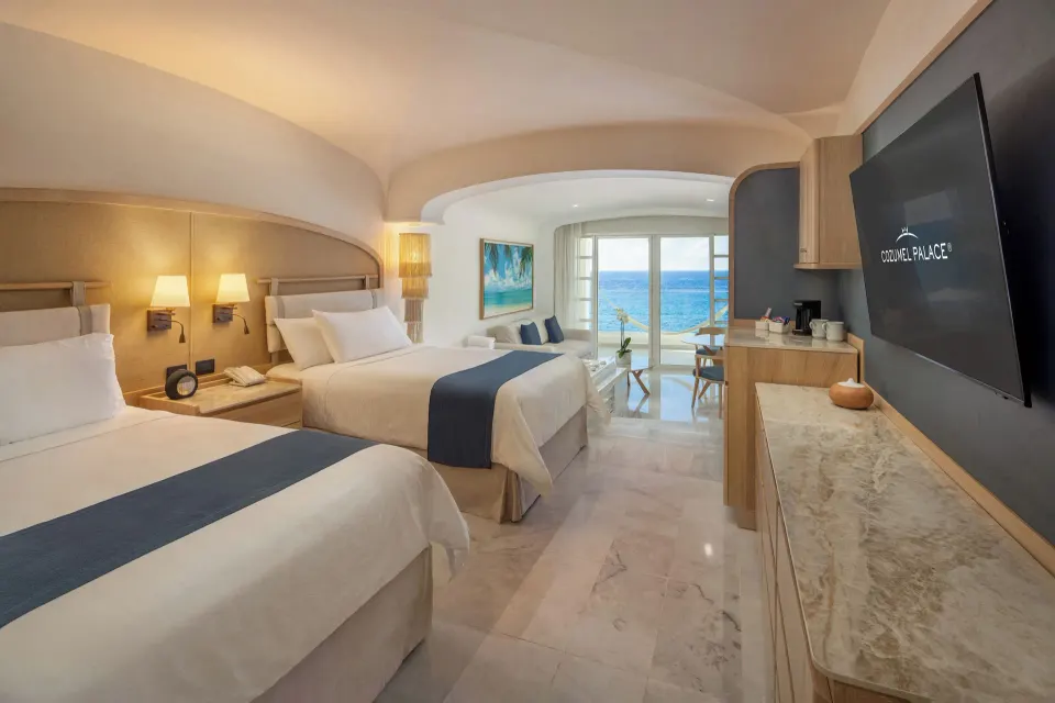 Two double beds and balcony doors framing ocean views at Cozumel Palace.