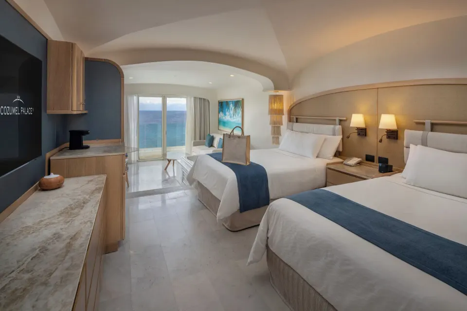 Two double beds with ocean view and seating area at Cozumel Palace.