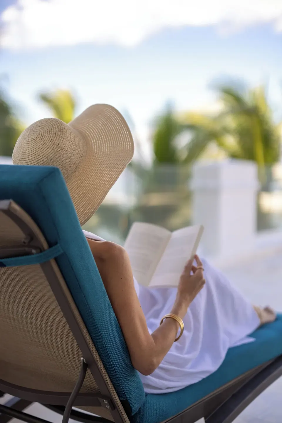Guest reading on a pool lounger under a sun hat at Cozumel Palace