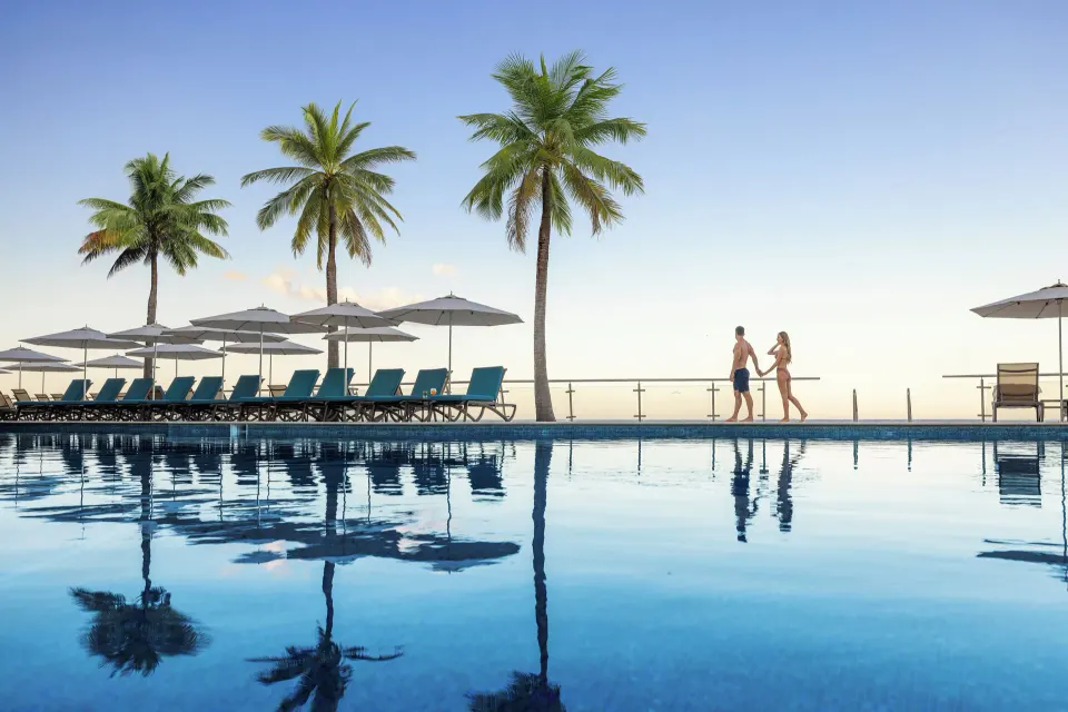Row of pool loungers and umbrellas with palm trees reflected in the infinity pool at Cozumel Palace
