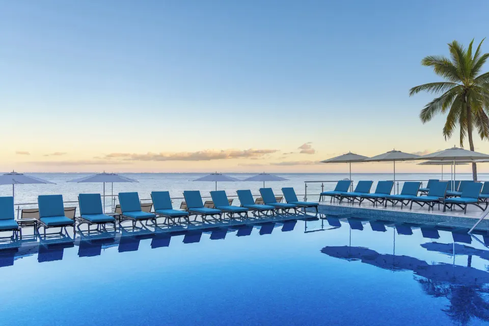 Infinity-edge pool lined with lounge chairs facing the sea at Cozumel Palace.