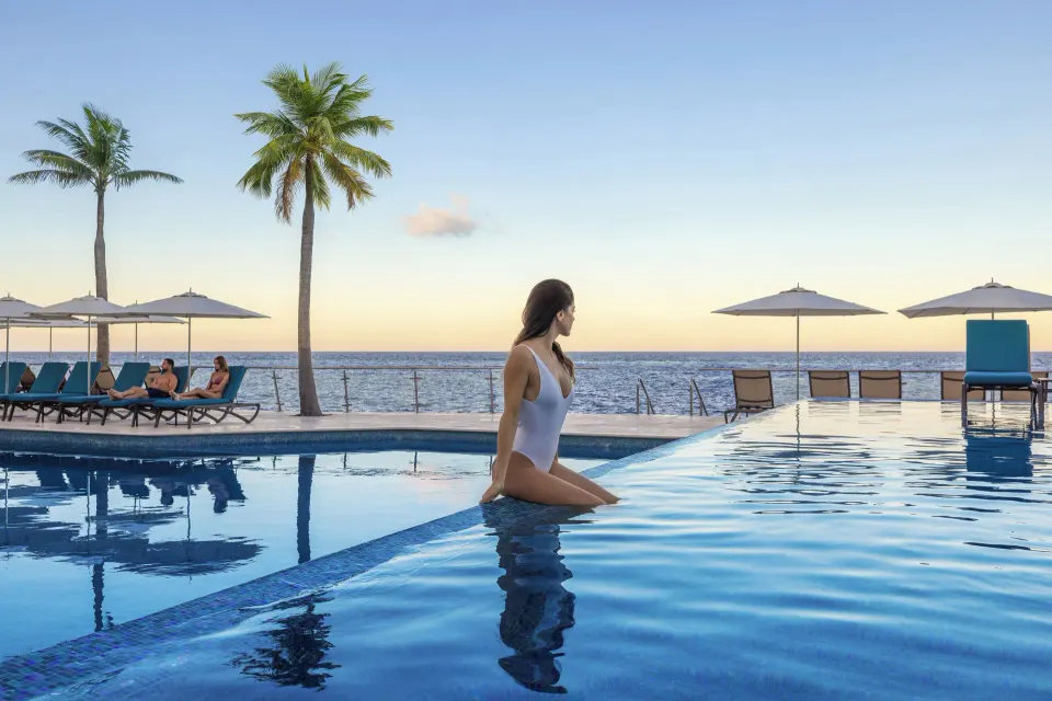 Woman kneeling on a ledge in the infinity pool at Cozumel Palace with ocean view