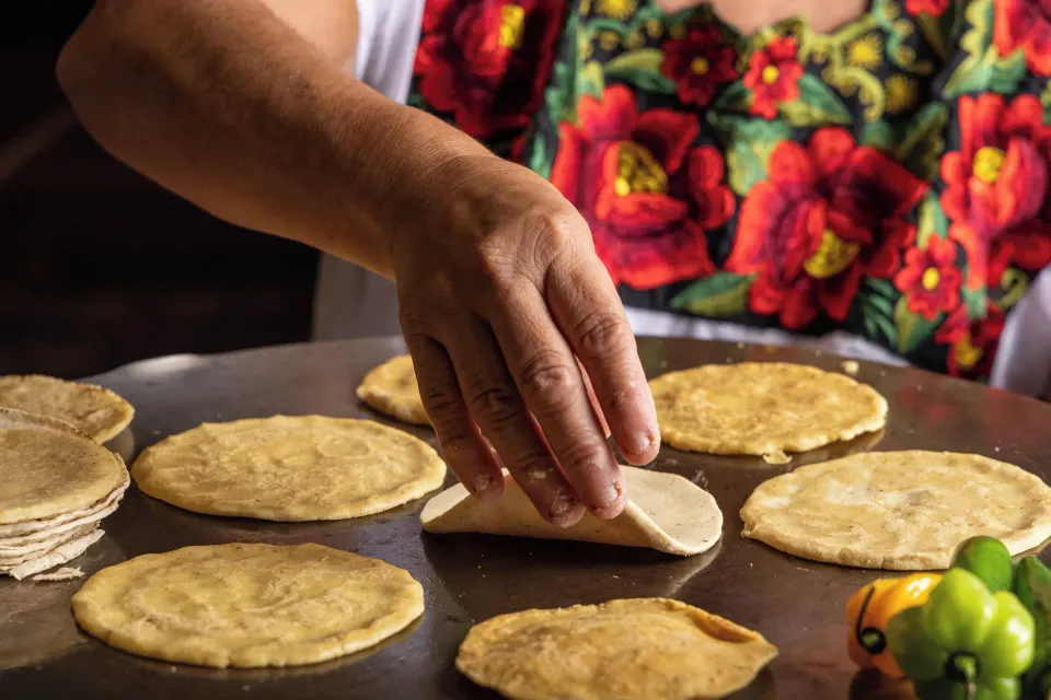 Hands preparing corn tortillas on a comal at Cozumel Palace