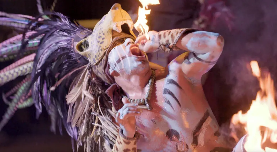 Costumed fire performer in tribal makeup breathing flame at Cozumel Palace