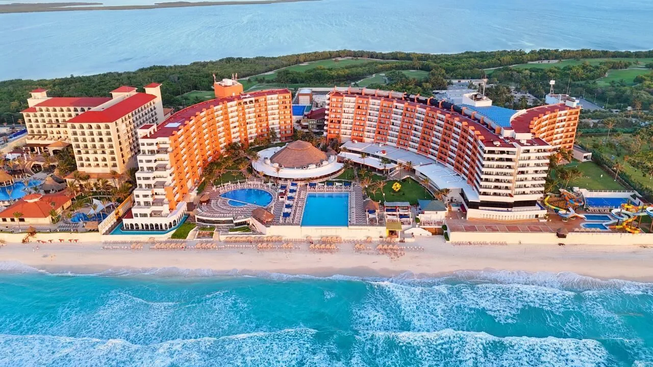 Aerial beachfront view of Crown Paradise Club Cancun with pools and curved hotel wings.