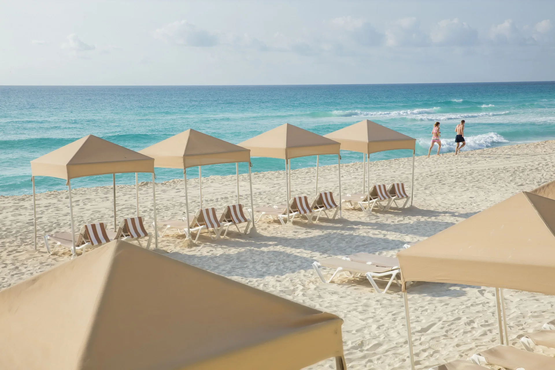 Beach cabanas and lounge chairs along turquoise water at Crown Paradise Club Cancun.