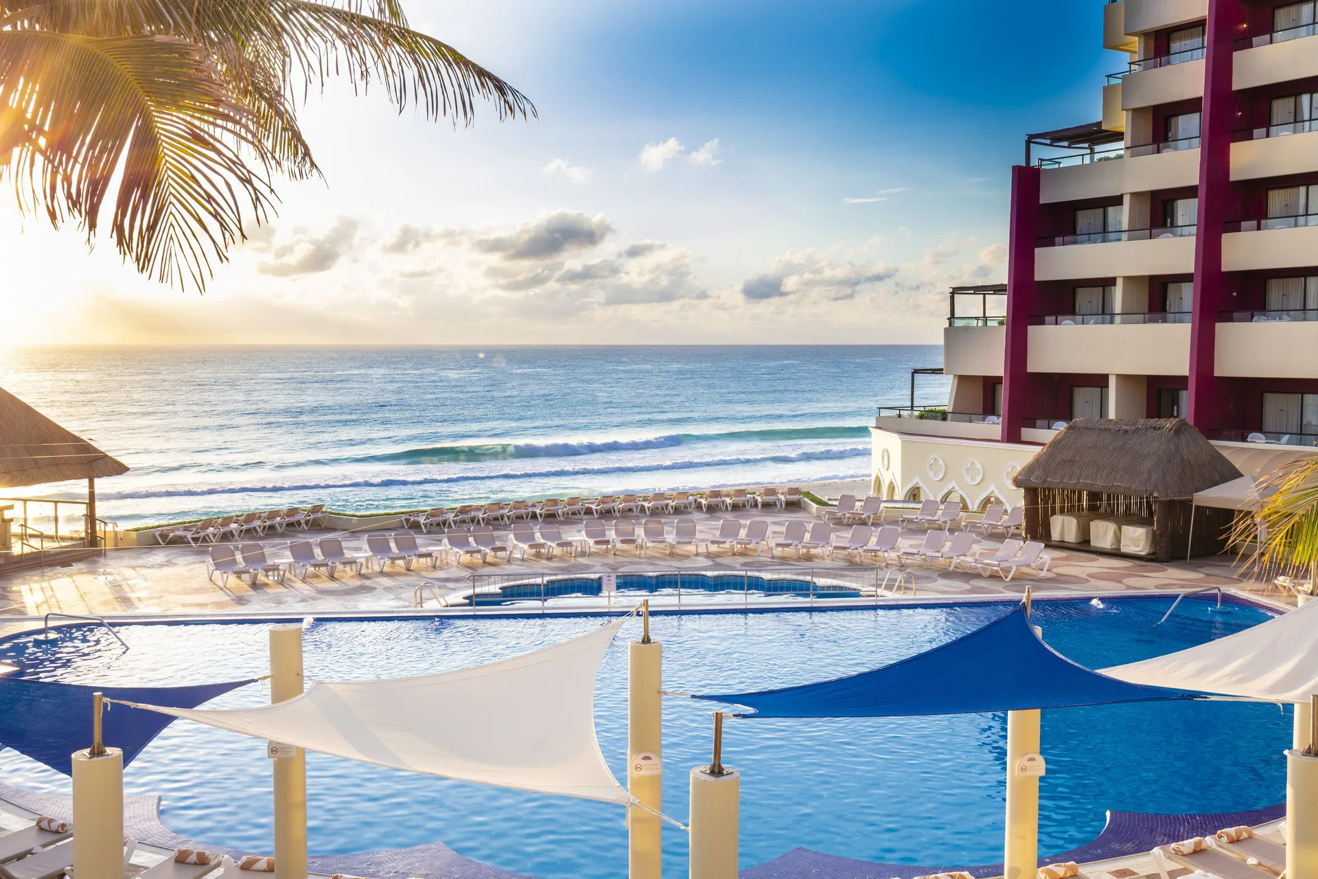 Beachfront pool at Crown Paradise Club Cancun with shade canopies, loungers, and ocean waves.