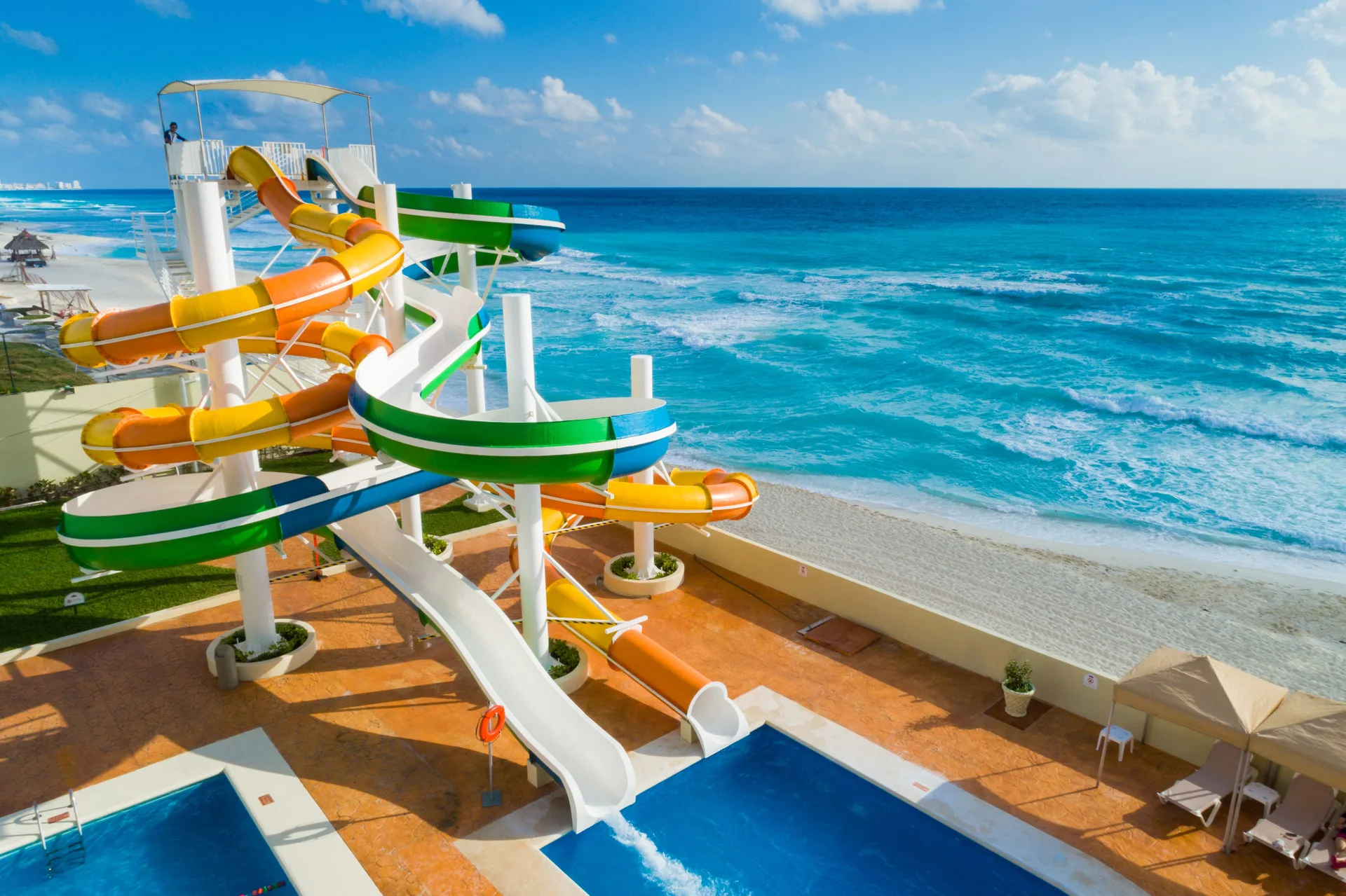 Colorful water slides at Crown Paradise Club Cancun beside the beach and turquoise sea.