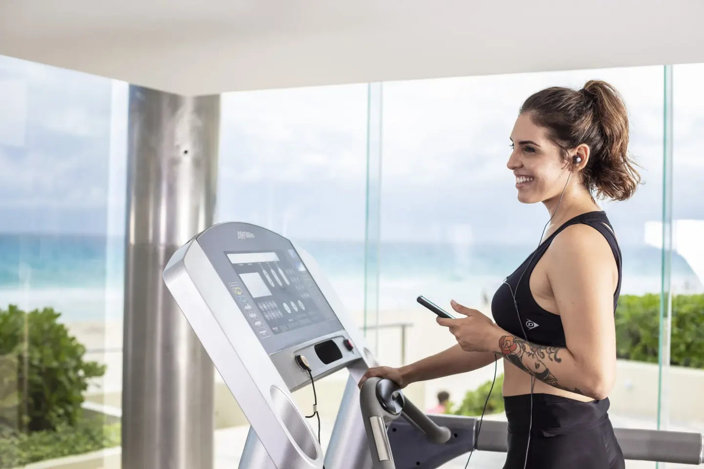 Guest using a cardio machine at Crown Paradise Club Cancun with beach view through windows.