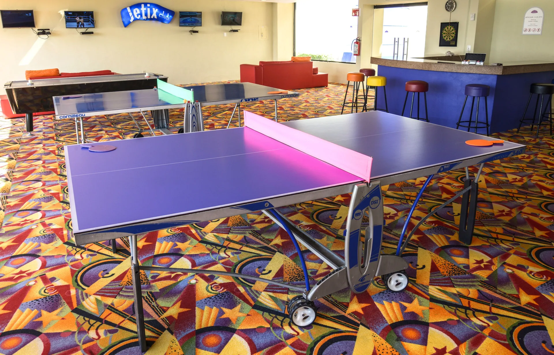 Game room with ping-pong tables, bar stools, and TVs at Crown Paradise Club Cancun.