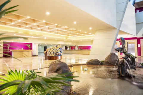 Lobby at Crown Paradise Club Cancun with reception desks, a water feature, and sculpture.