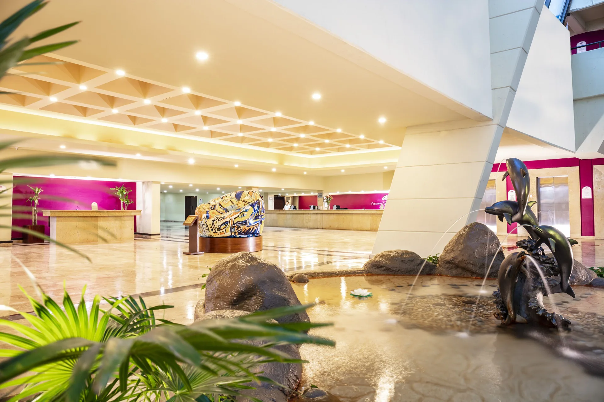 Lobby at Crown Paradise Club Cancun with reception desks, a water feature, and sculpture.