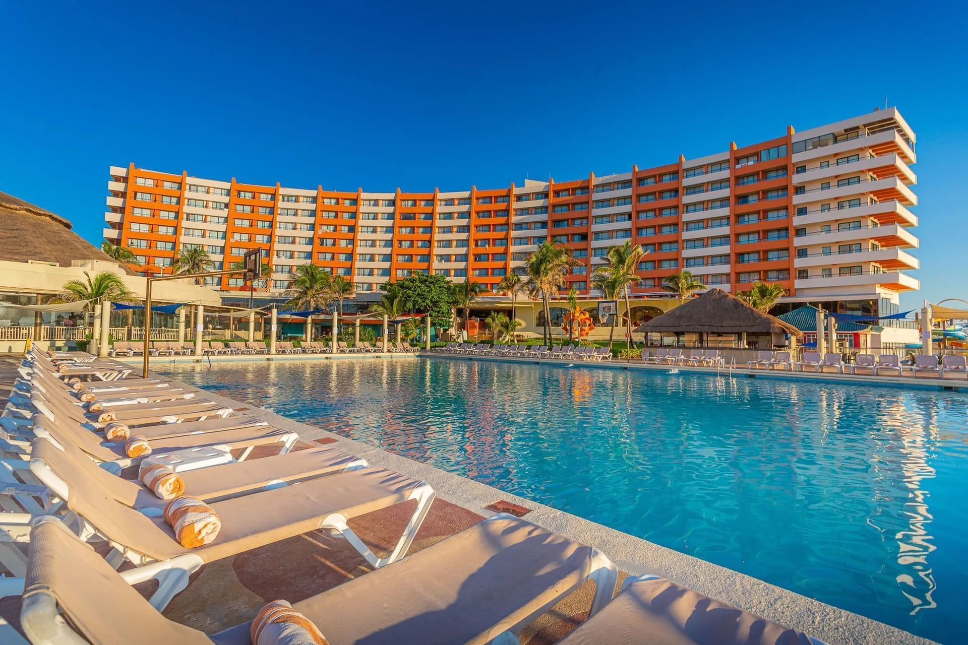 Main pool at Crown Paradise Club Cancun with rows of loungers and the hotel tower behind it.