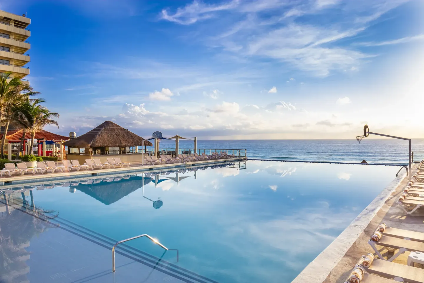Main pool at Crown Paradise Club Cancun with loungers, basketball hoops, and ocean views.