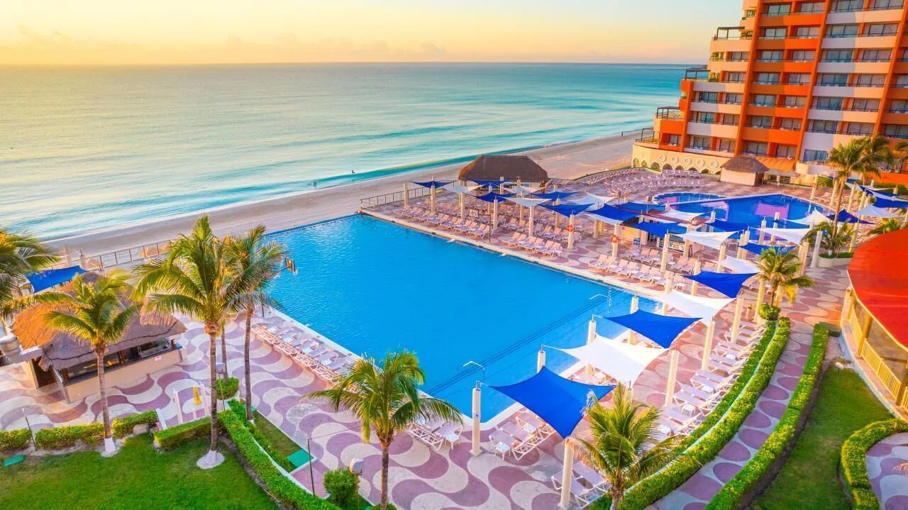 Oceanfront pool and beach at Crown Paradise Club Cancun with loungers, shade sails, and palms.