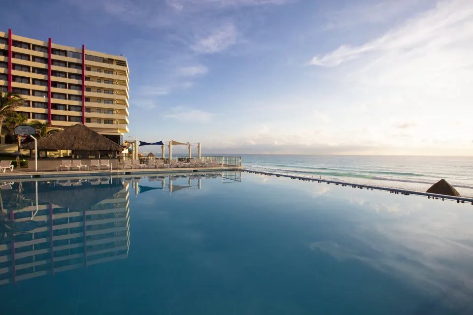Oceanfront pool and hotel tower at Crown Paradise Club Cancun with beach beyond.