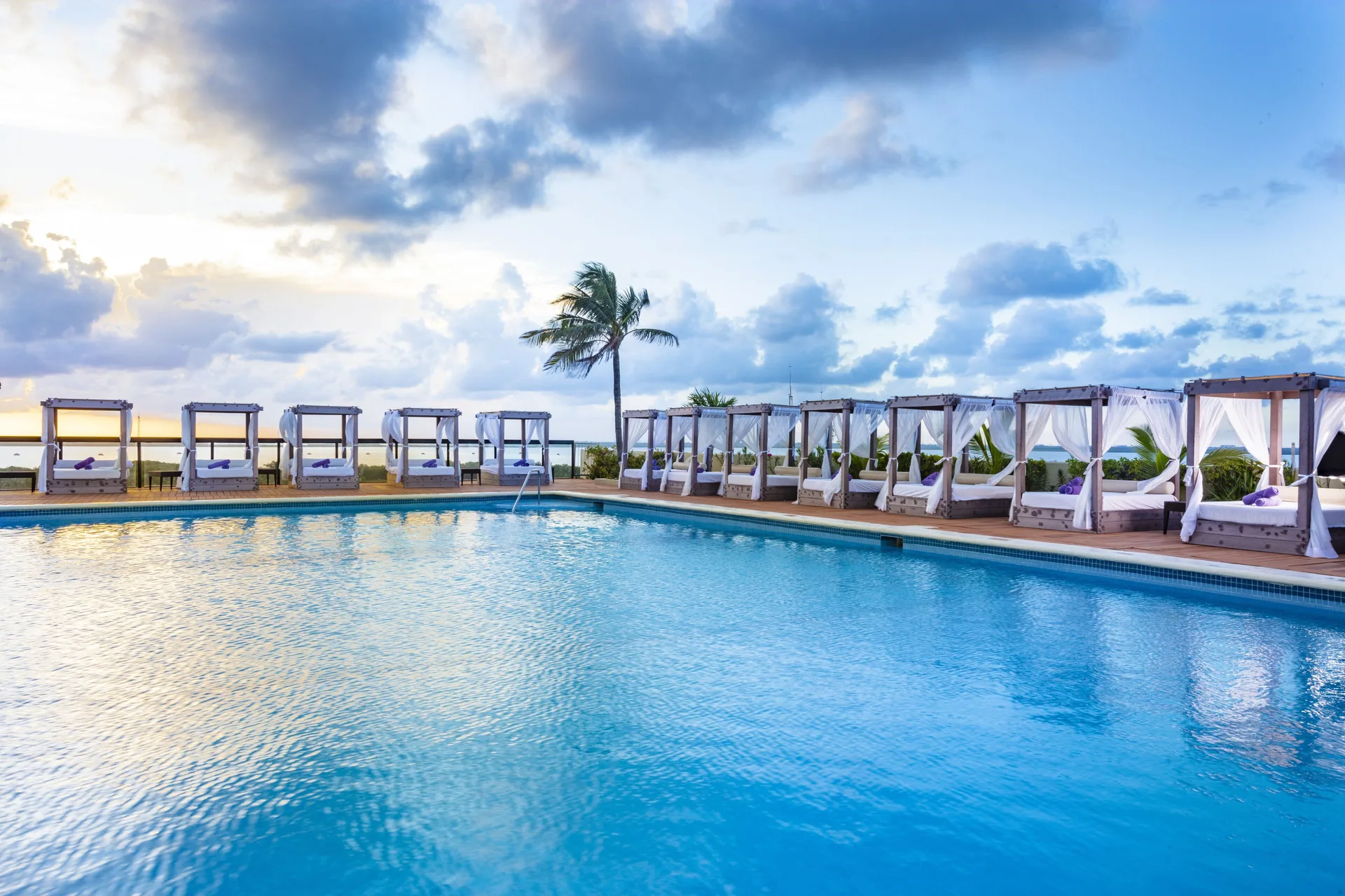 Poolside cabanas at Crown Paradise Club Cancun line the water under a cloudy sky.
