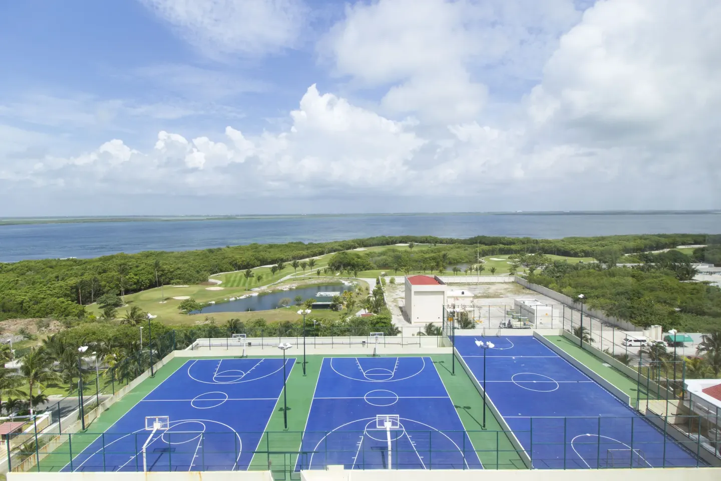 Blue sports courts with lagoon and green fairways beyond at Crown Paradise Club Cancun.