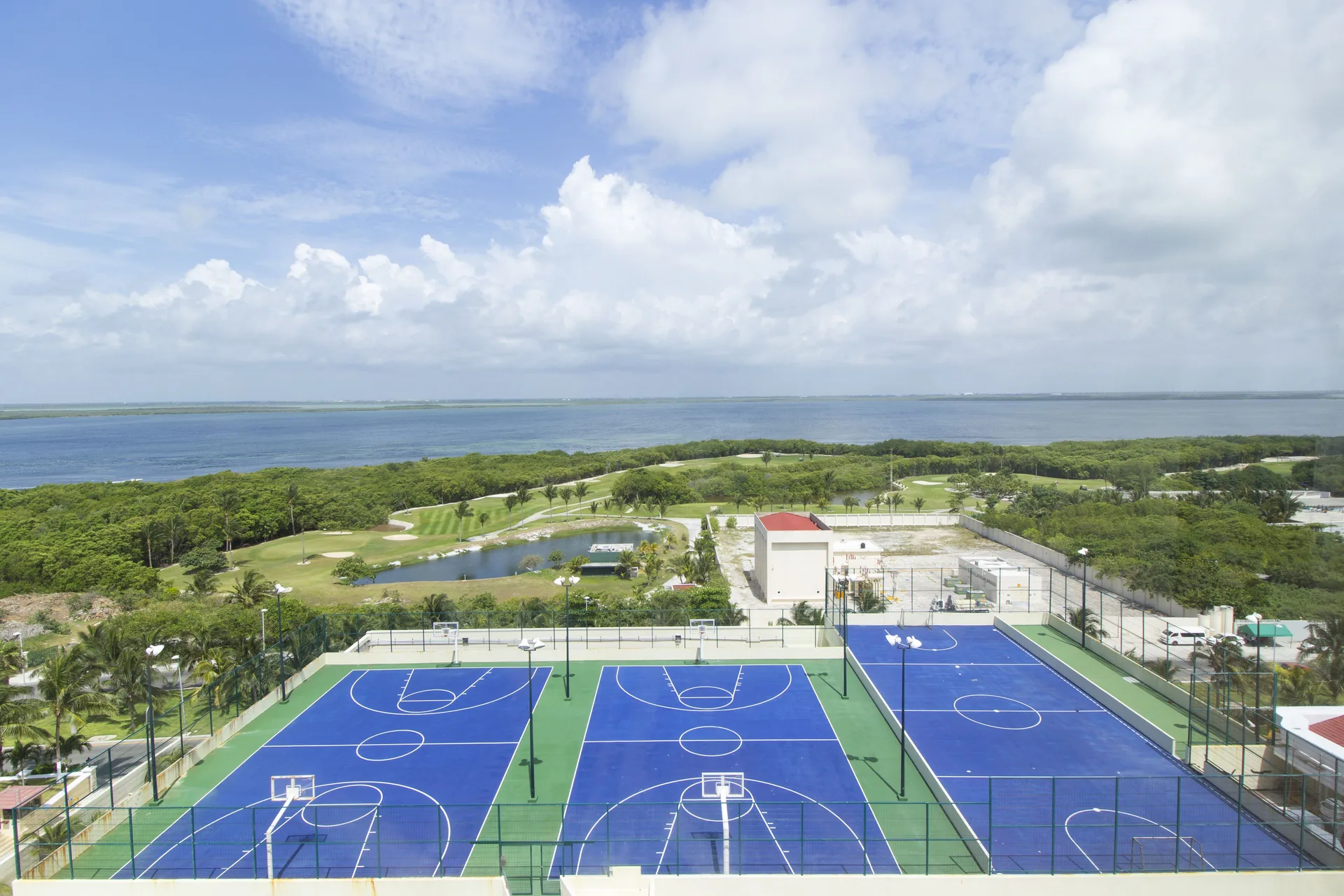 Blue sports courts with lagoon and green fairways beyond at Crown Paradise Club Cancun.