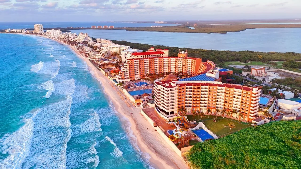 Wide aerial coastline view of Crown Paradise Club Cancun beside the beach and lagoon.