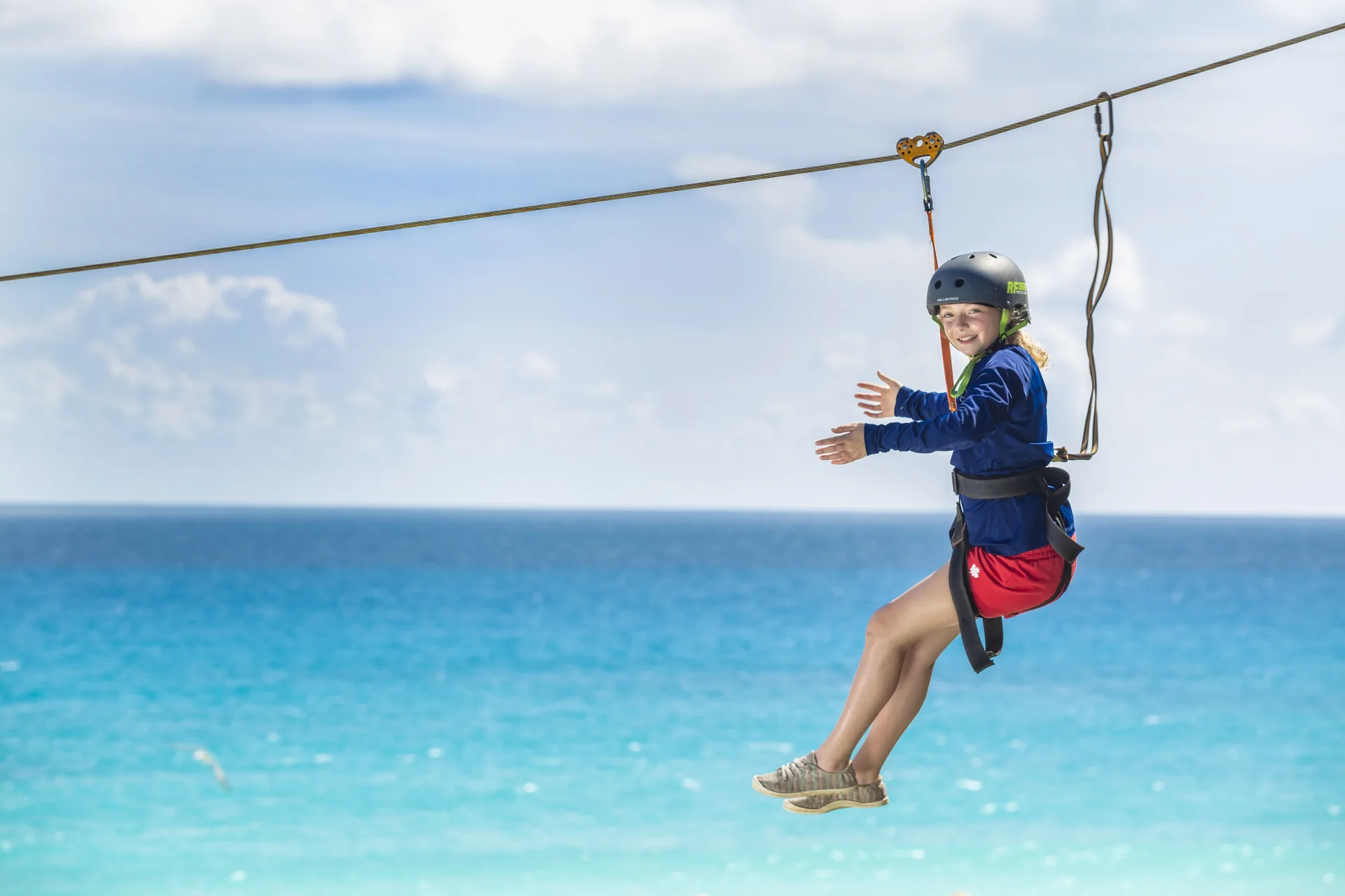 Child on a zip line above turquoise water at Crown Paradise Club Cancun.