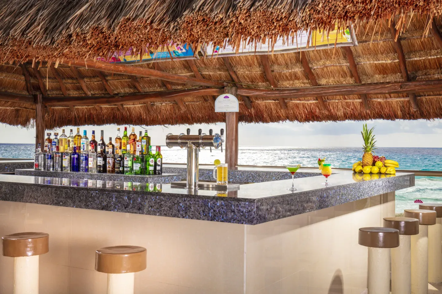 Thatched beach bar with ocean view and colorful drinks at Crown Paradise Club Cancun.