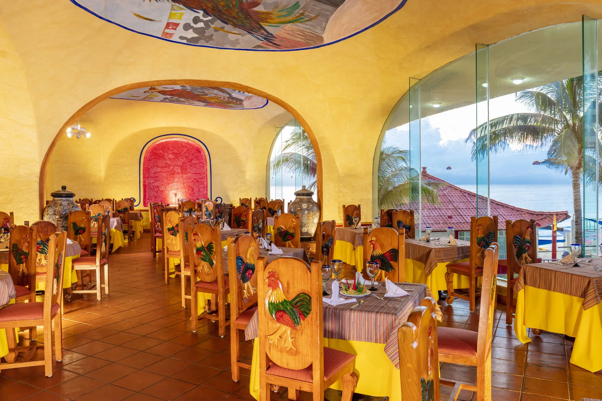 Colorful Mexican dining room at Crown Paradise Club Cancun with rooster-painted chairs and ocean views.