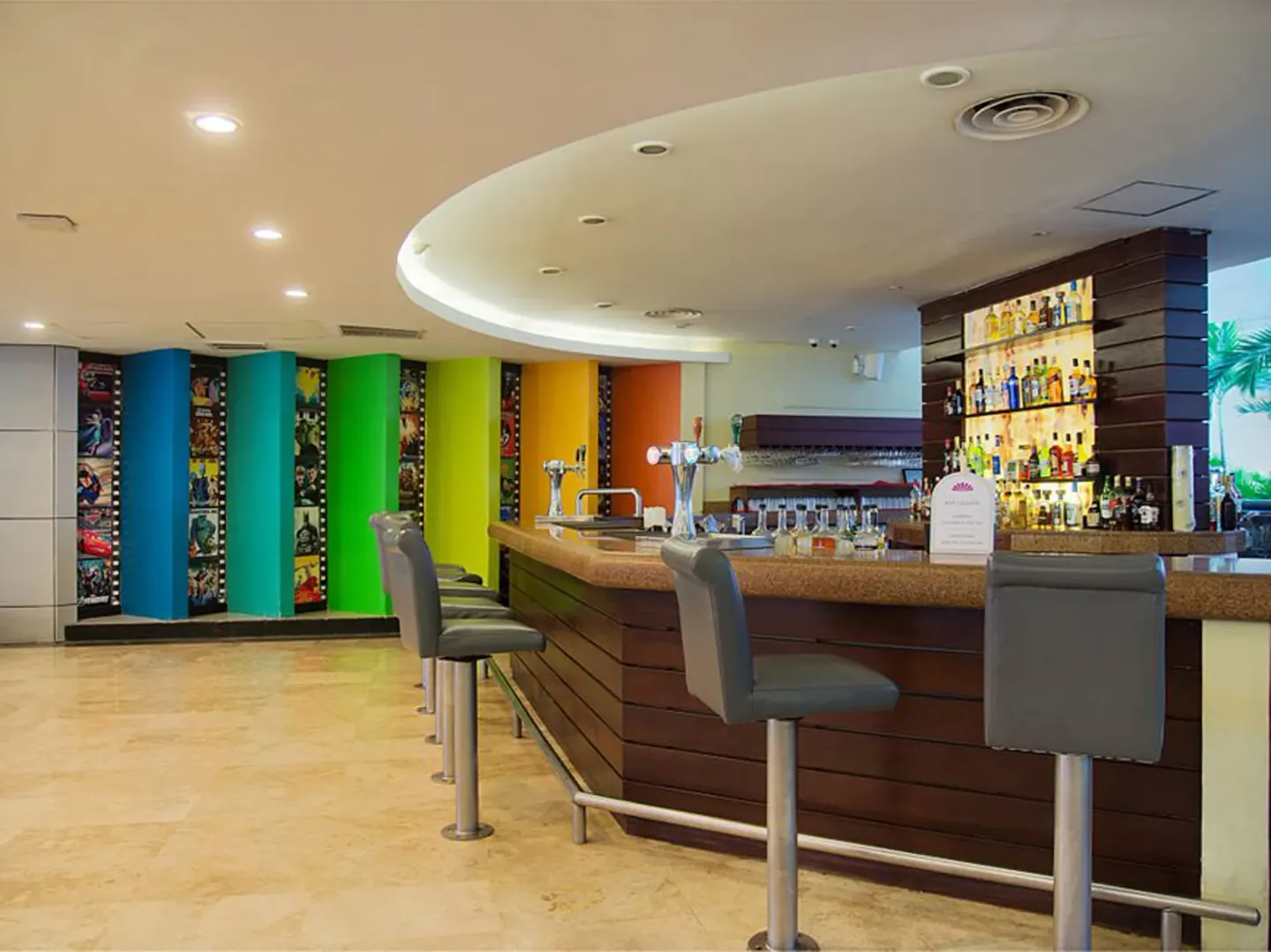 Modern bar at Crown Paradise Club Cancun with colorful wall panels, bar stools, and backlit bottles.