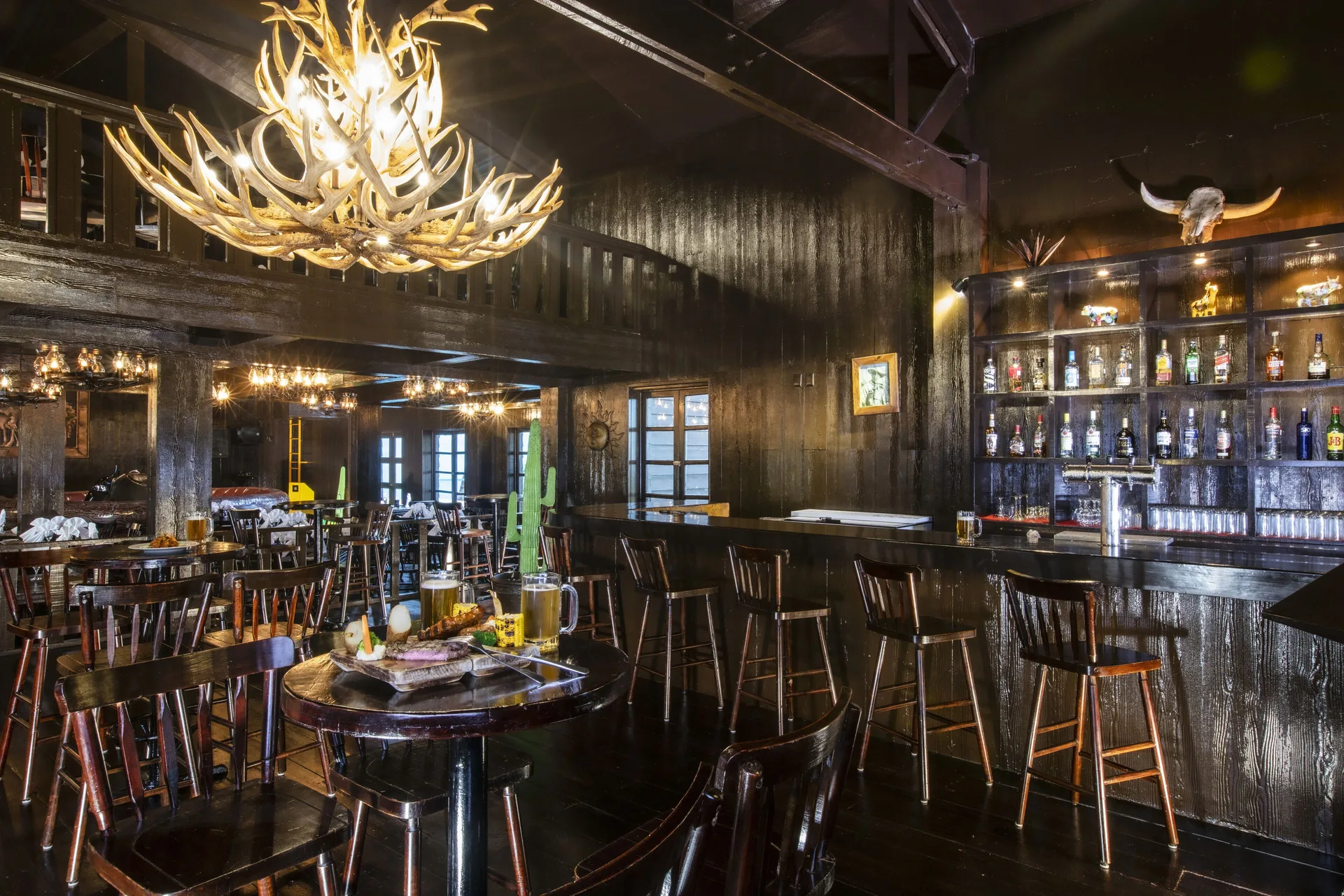 Dark wood bar with antler chandelier at Crown Paradise Club Cancun.