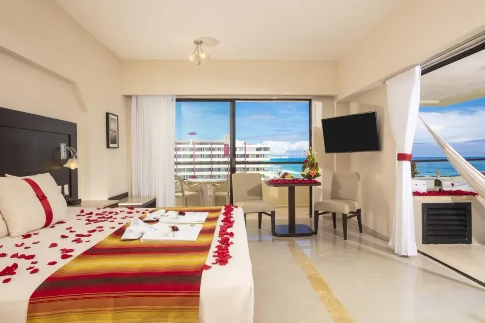 Honeymoon Room king bed with rose petals, seating, and balcony views at Crown Paradise Club Cancun.