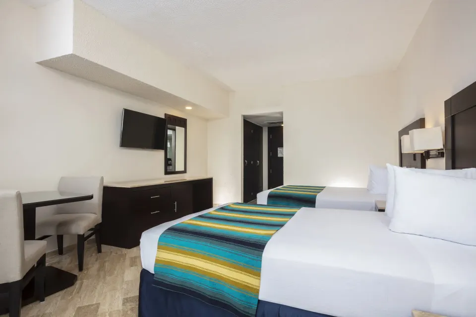Standard Ocean View room with two beds, desk, mirror, and TV at Crown Paradise Club Cancun.