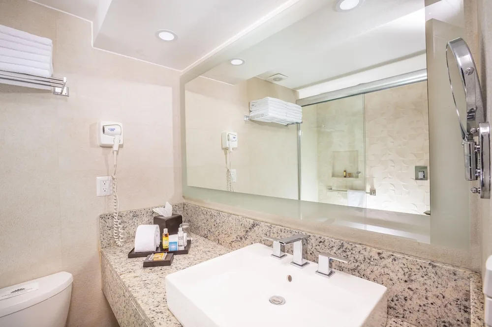 Standard Room bathroom vanity, mirror and glass shower at Crown Paradise Club Cancun.