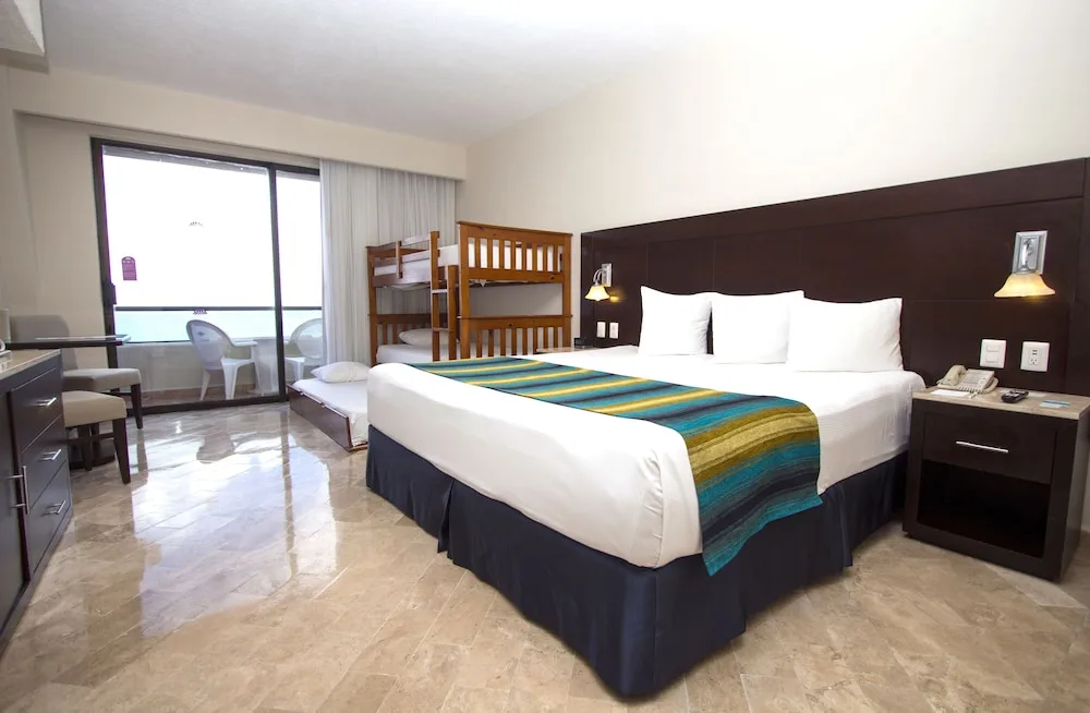 Standard Room with king bed, bunk beds, tile floor and balcony at Crown Paradise Club Cancun.