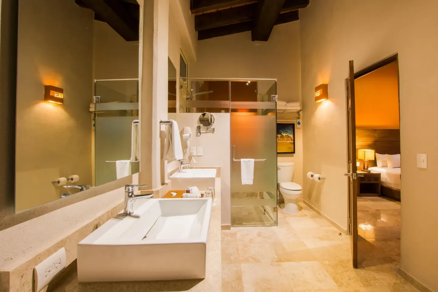 Bathroom with double vanity and shower beside a bedroom at Crown Paradise Club Puerto Vallarta.