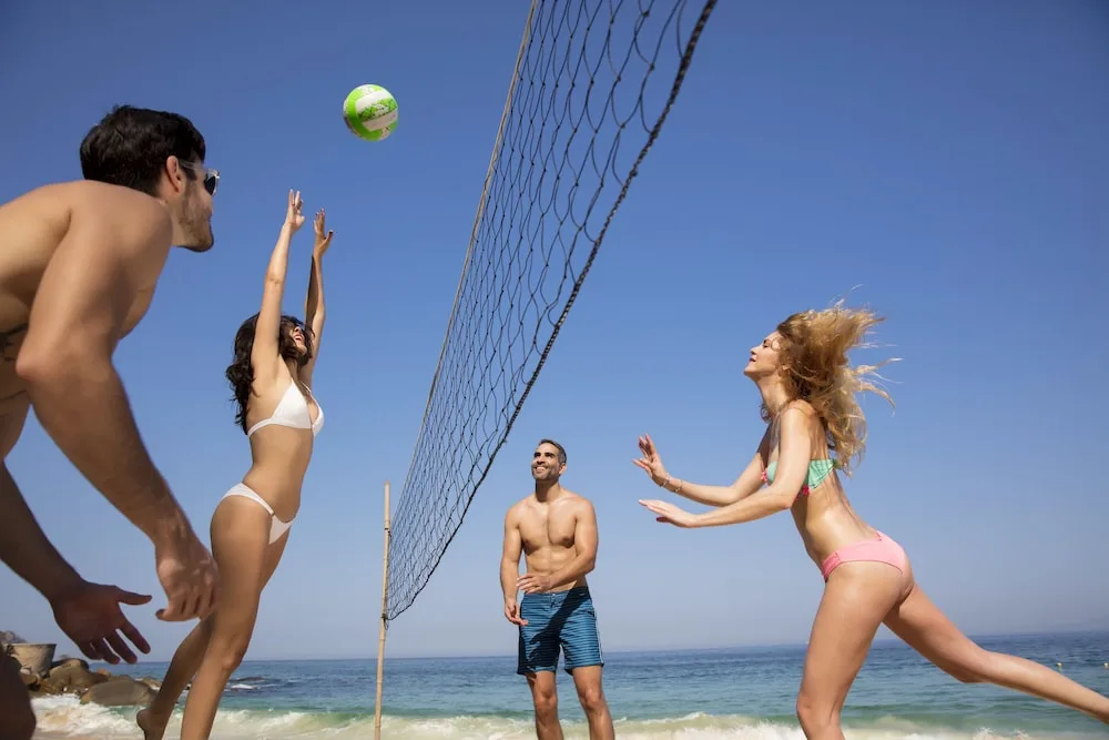 Guests playing beach volleyball by the ocean at Crown Paradise Club Puerto Vallarta.