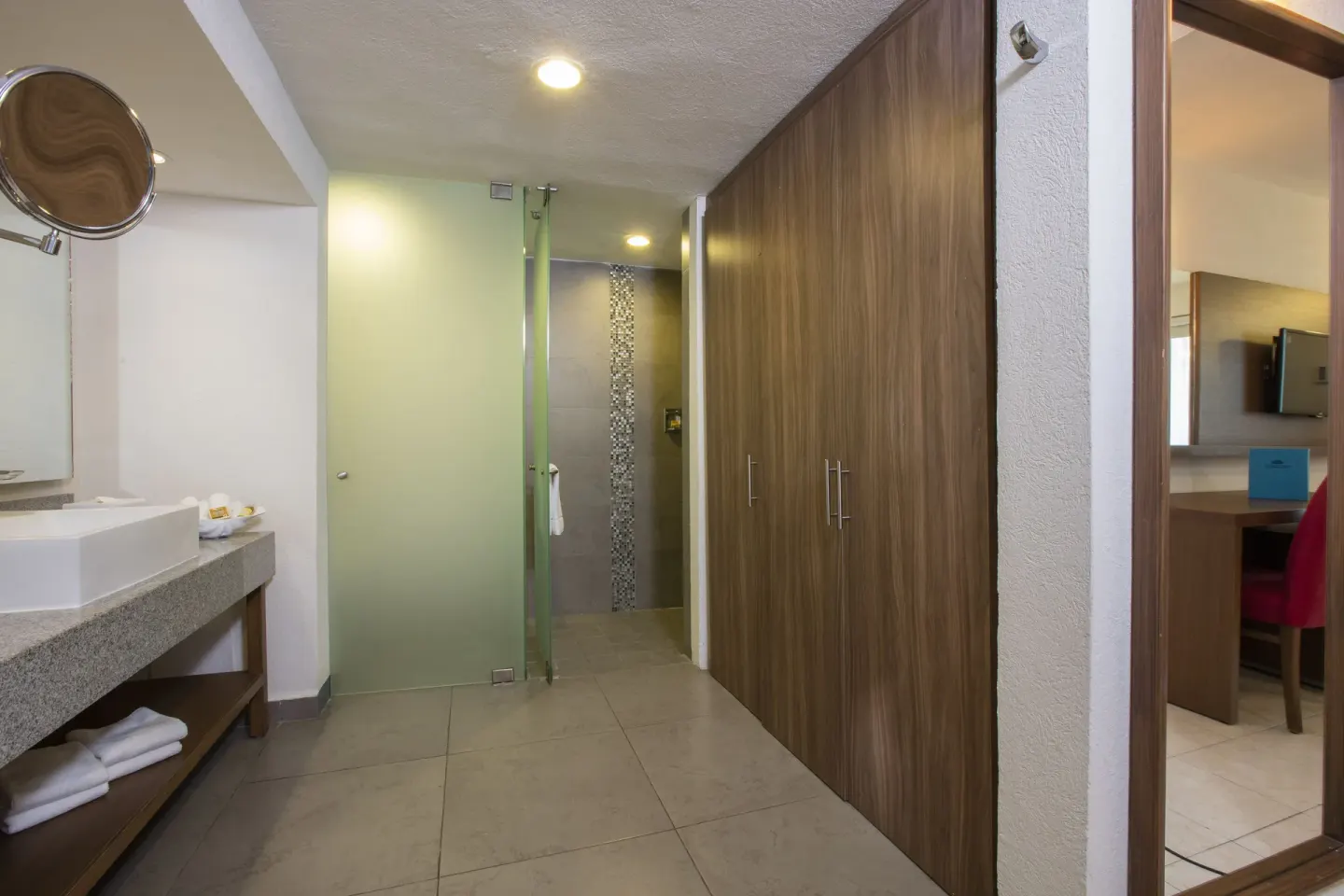 Guest room bathroom vanity, glass shower and wood closet doors at Crown Paradise Club Puerto Vallarta.